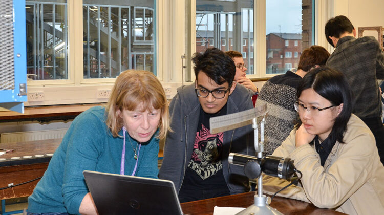 A professor pointing out something on a laptop screen to 2 students in a lab.