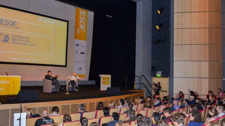 Matthew Cobb and Brian Cox sat on a stage at the Euroscience Open Forum, Manchester 2016, giving a talk to a packed lecture theatre.