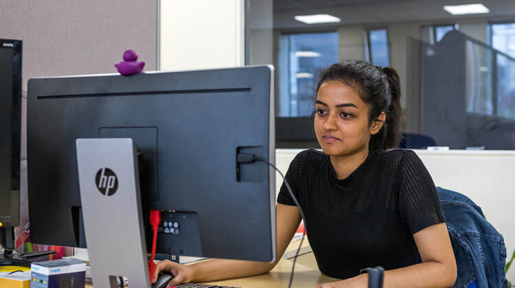 Student looking at computer with one hand on the mouse, the other on the keyboard.