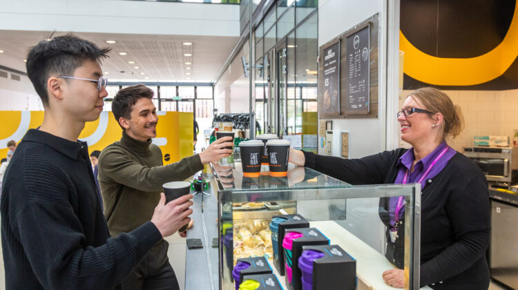 Students being handed coffee over the counter at Code Cafe in the Alan Turing Building.