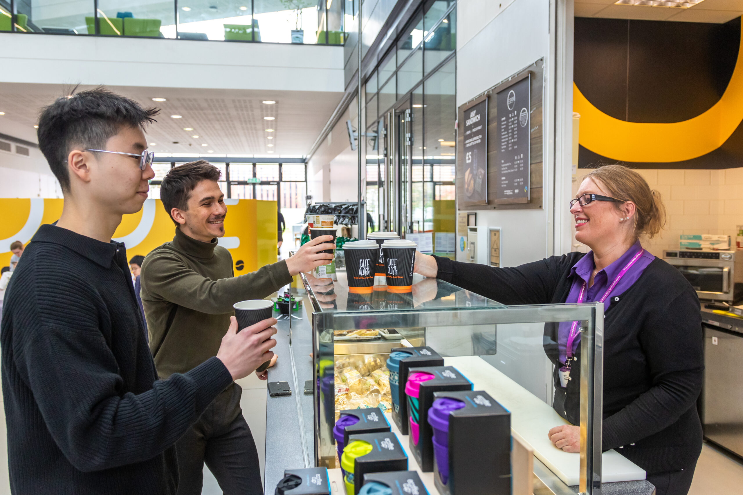 Students being handed coffee over the counter at Code Cafe in the Alan Turing Building.